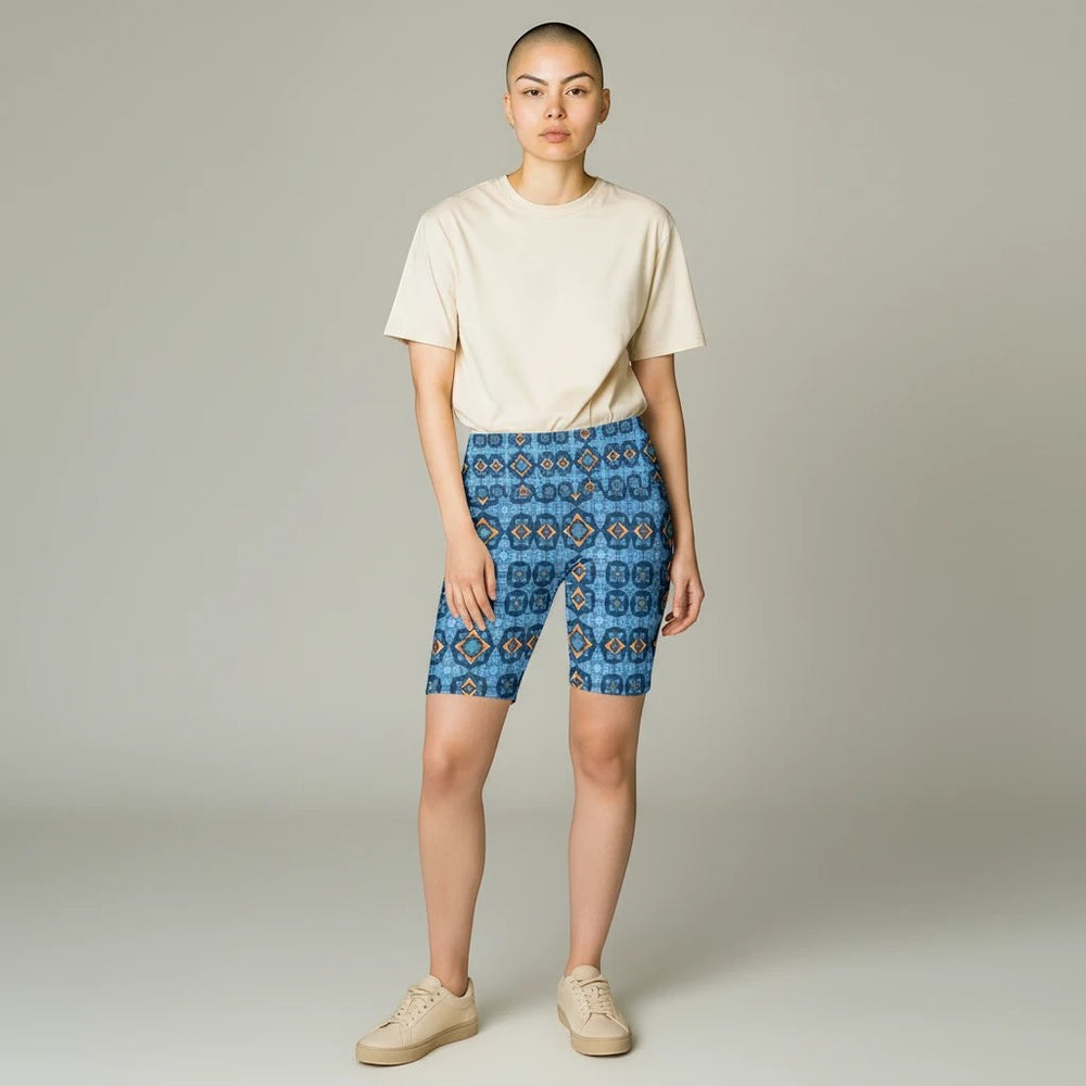 Model wearing Sea Dragon Dreams Goddess Isis workout shorts with a blue geometric pattern and a beige t-shirt.