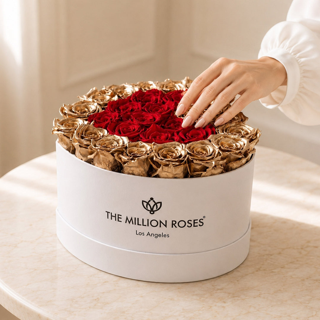 Sea Dragon Dreams heart-shaped white box filled with preserved red roses and 24K gold roses, touched by a hand.