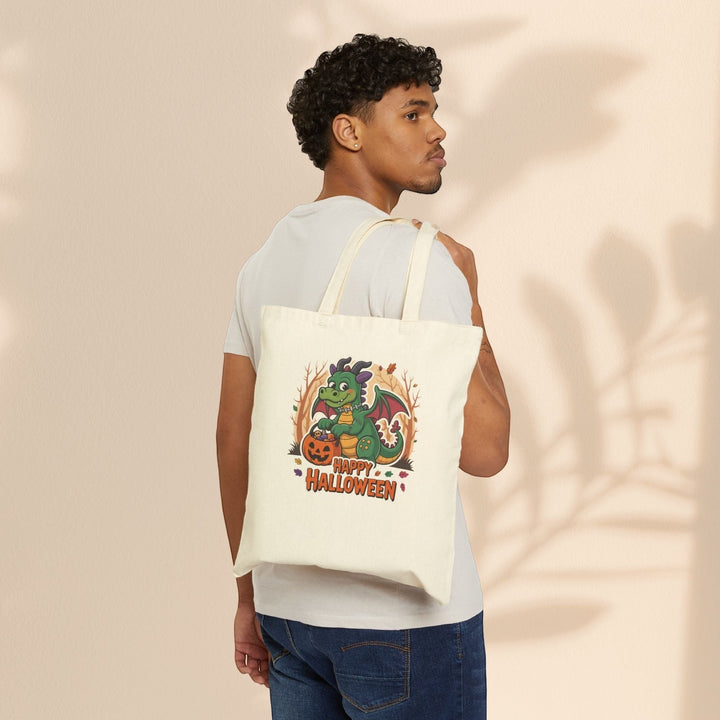 Man carrying a Sea Dragon Dreams natural cotton canvas tote bag with a cute Halloween dragon and pumpkin graphic.