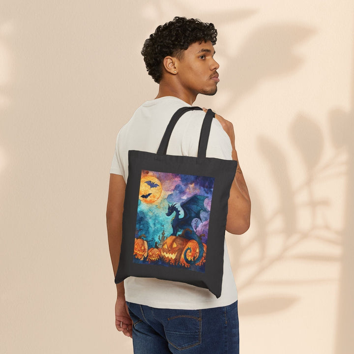 A man wearing a white t-shirt carries a Sea Dragon Dreams black cotton canvas tote bag with a Halloween dragon print.