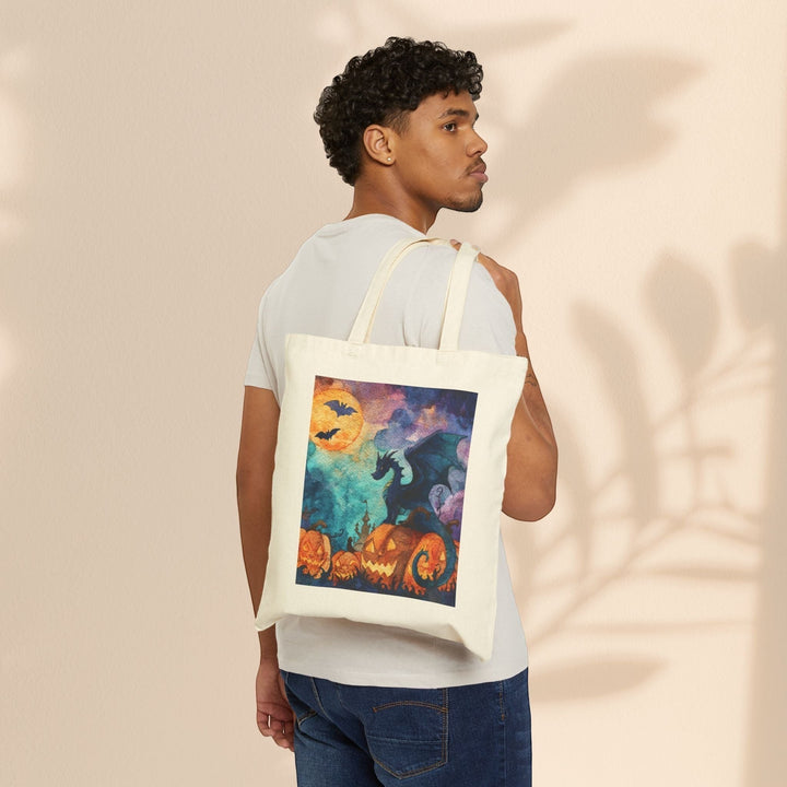 A man wearing a white t-shirt carries a Sea Dragon Dreams cotton canvas tote bag with a spooky dragon Halloween print.