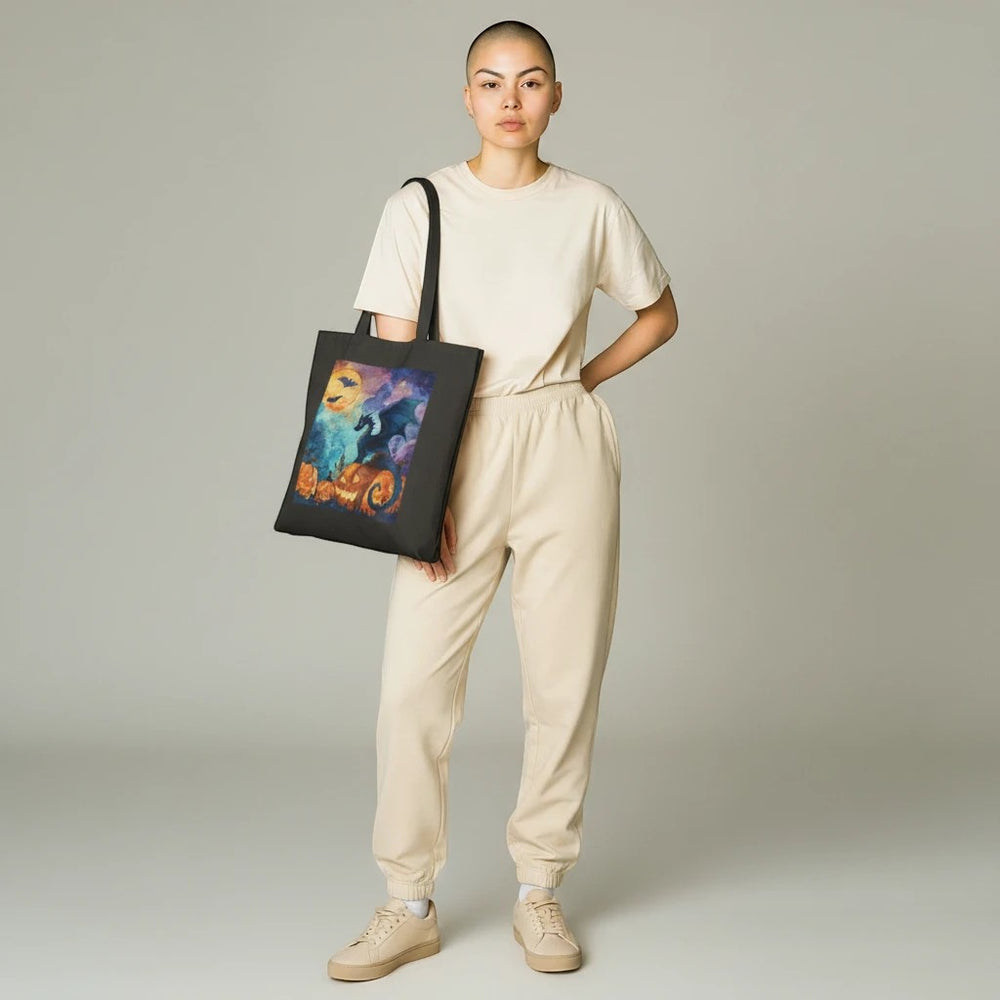 A person wearing a beige outfit carries a black Sea Dragon Dreams cotton canvas tote bag with a Halloween dragon print.