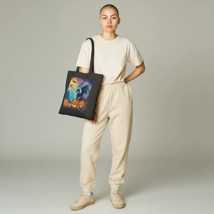 A person wearing a beige outfit carries a black Sea Dragon Dreams cotton canvas tote bag with a Halloween dragon print.