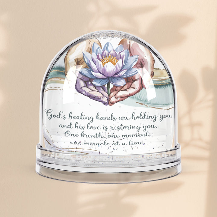 Sea Dragon Dreams inspirational snow globe featuring a lotus flower held by hands and the quote God’s Healing Hands Are Holding You.