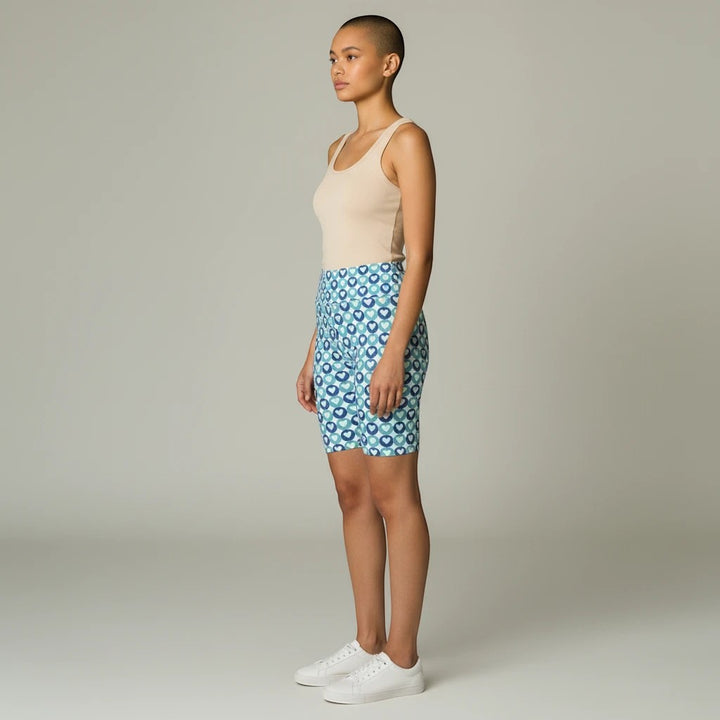Model wearing Sea Dragon Dreams blue heart pattern polyester workout shorts with a beige tank top and white sneakers.