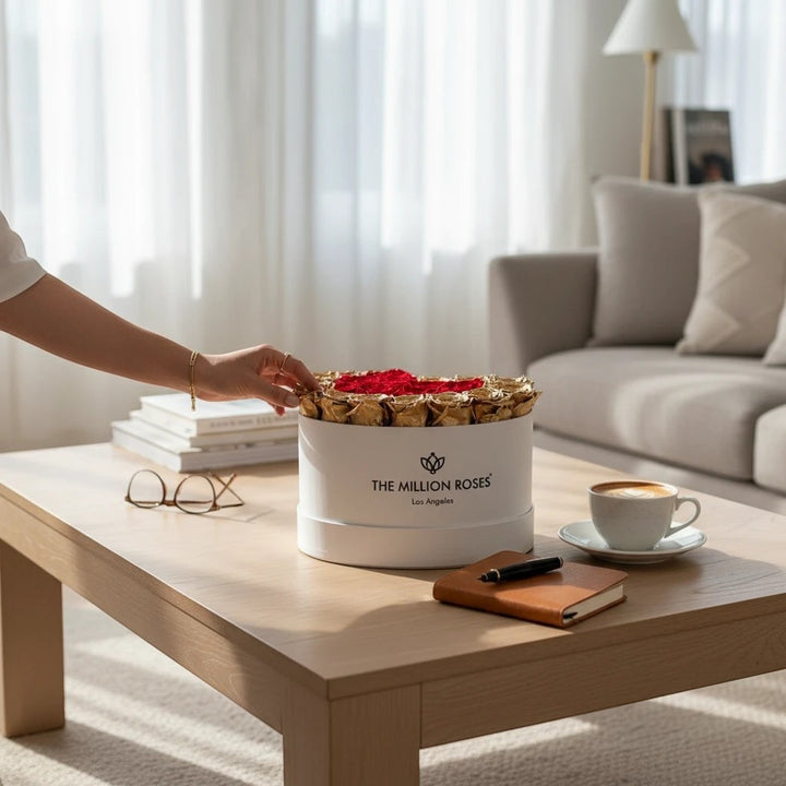 Sea Dragon Dreams heart-shaped white box filled with preserved red and 24K gold roses on a wooden coffee table.
