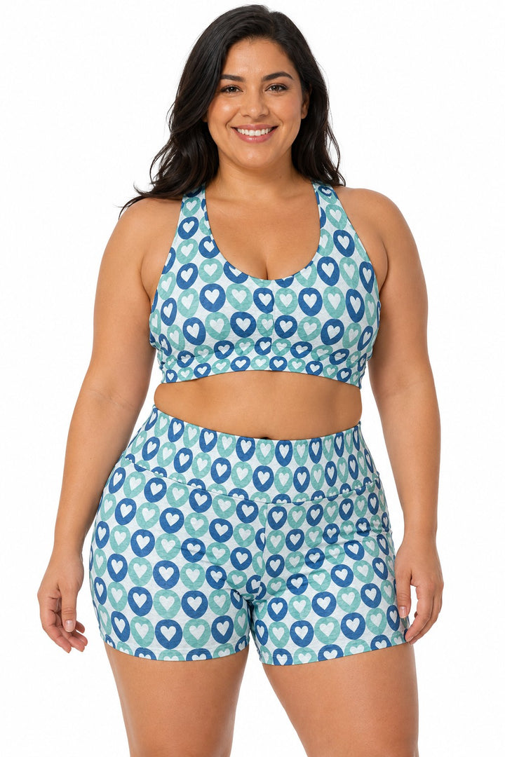 A smiling woman wearing a Sea Dragon Dreams sports bra and high-waisted shorts set with a blue and white heart pattern.