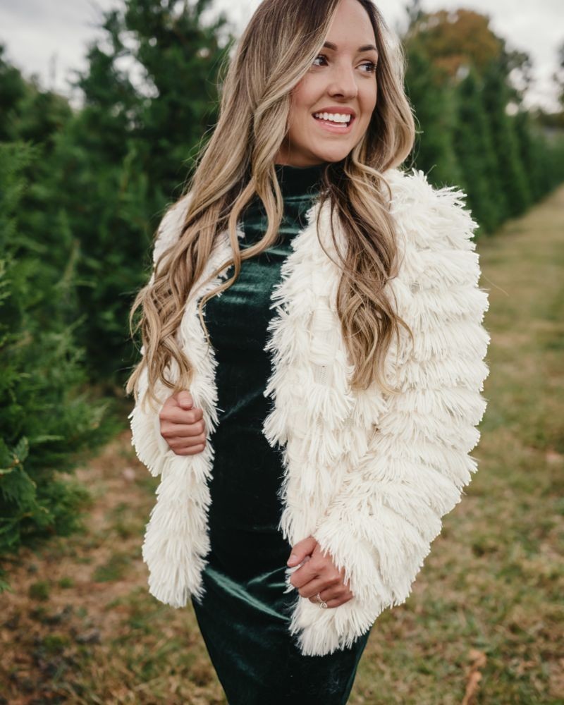 Sea Dragon Dreams ivory faux shag layered jacket worn by a woman over a dark green velvet dress in a tree farm.