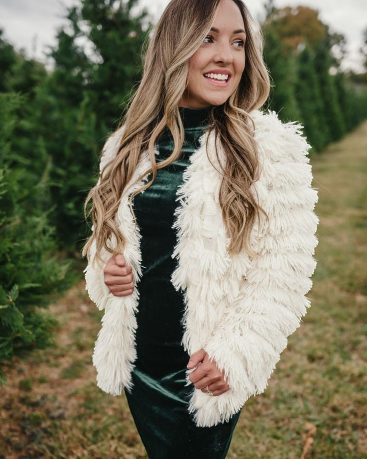 Sea Dragon Dreams ivory faux shag layered jacket worn by a woman over a dark green velvet dress in a tree farm.