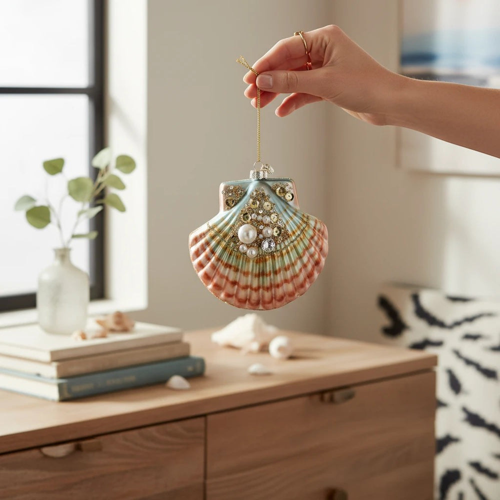 Sea Dragon Dreams Mark Roberts jeweled clam shell ornament held by hand against a coastal-themed room background.