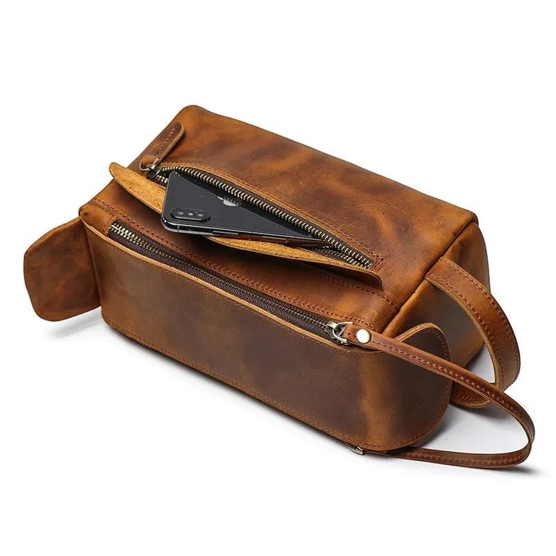 Sea Dragon Dreams brown handmade leather dopp kit with a zippered front pocket holding a smartphone