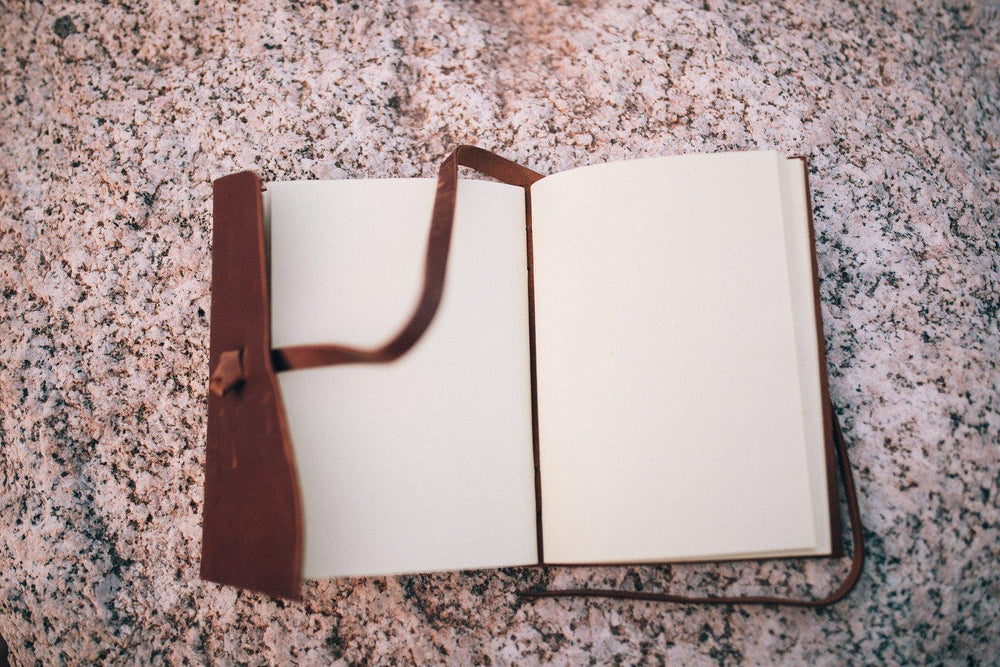 Sea Dragon Dreams Kodiak leather travel journal with blank handmade artisan paper pages resting on a stone surface.