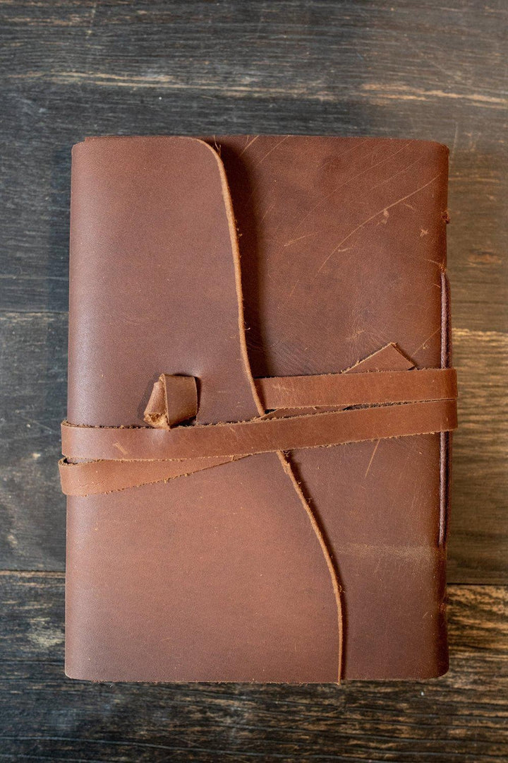 Sea Dragon Dreams Kodiak leather travel journal with a rustic brown wrap-around tie closure on a dark wooden surface.