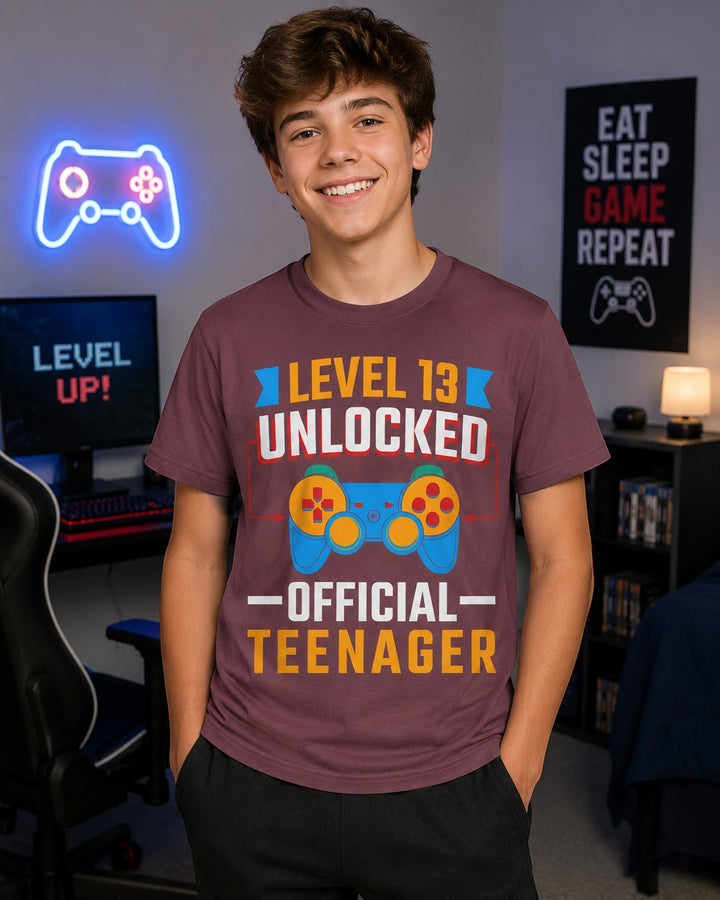 A smiling teenager wearing a maroon Sea Dragon Dreams Level 13 Unlocked gamer t-shirt in a gaming room.