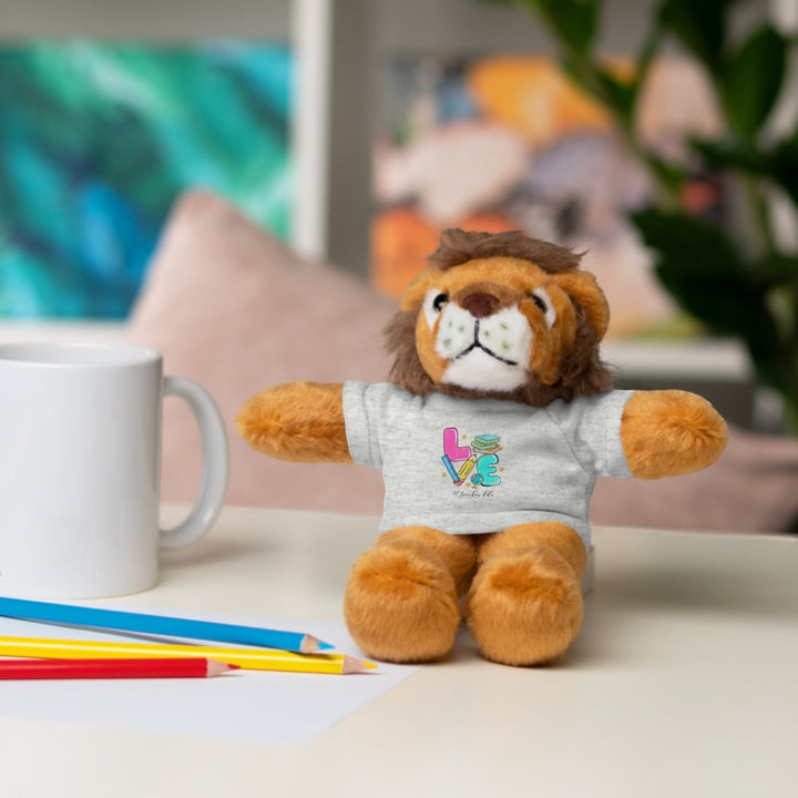 Sea Dragon Dreams lion plush toy wearing a grey t-shirt with Love Teacher Life graphic on a desk with colored pencils