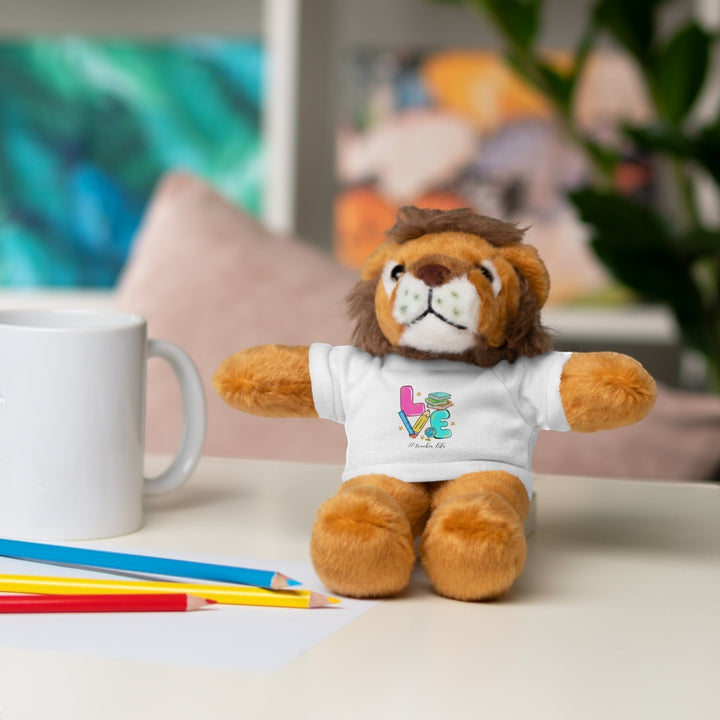 Sea Dragon Dreams lion plush toy wearing a white t-shirt with Love Teacher Life graphic, sitting on a desk.