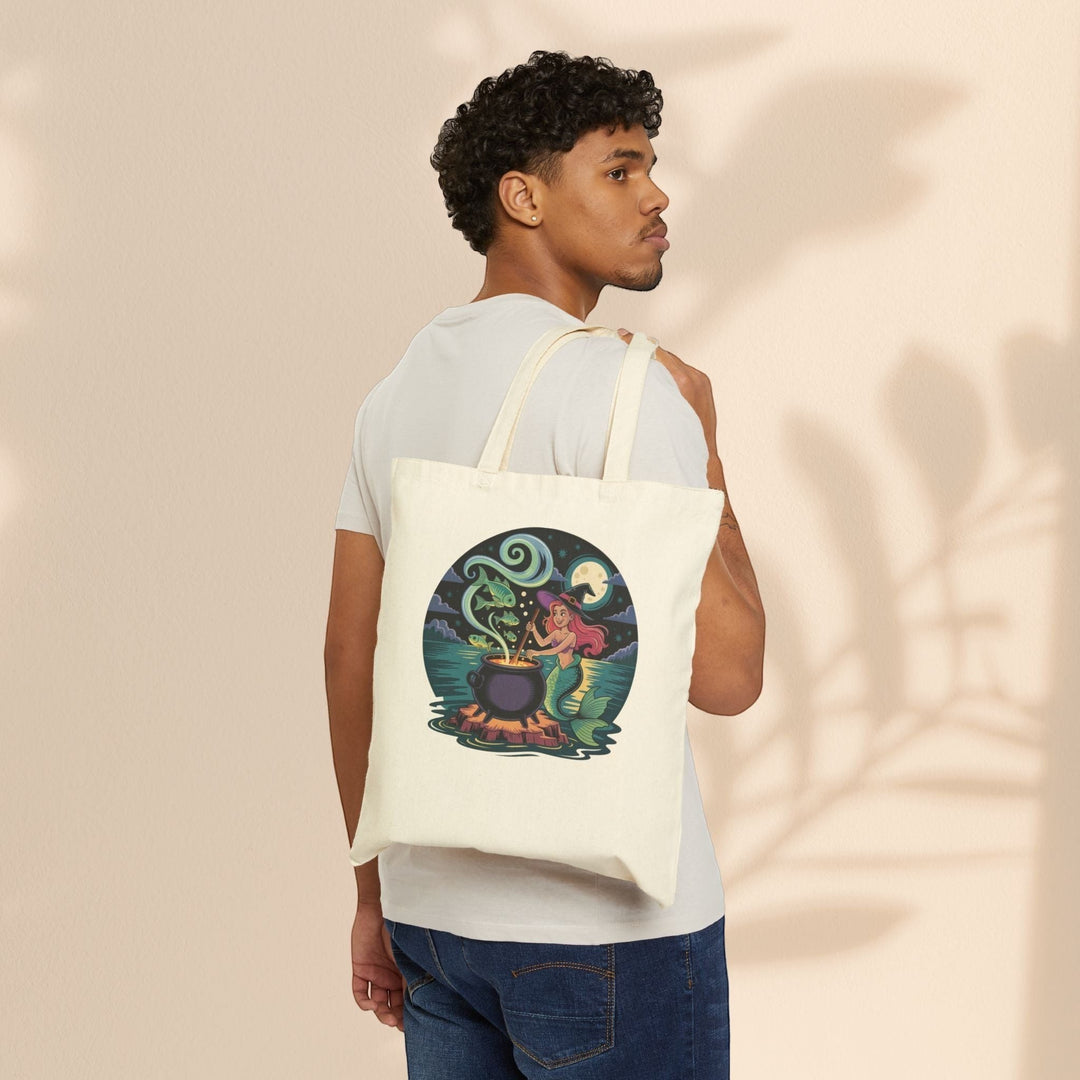 Sea Dragon Dreams cotton canvas tote bag with mermaid cauldron graphic worn over the shoulder by a man.