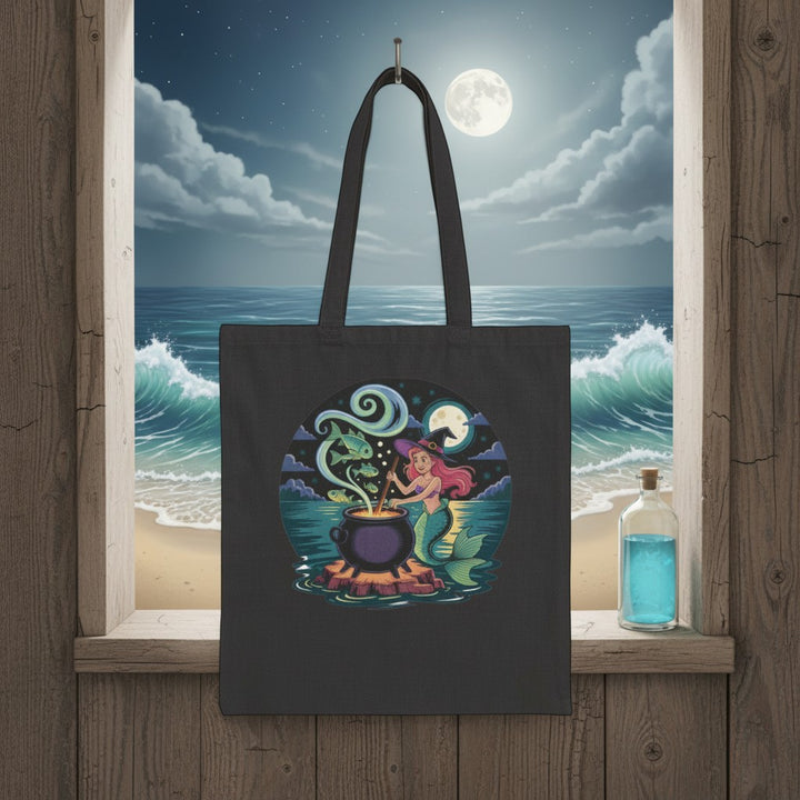 Sea Dragon Dreams black cotton canvas tote bag featuring a whimsical mermaid stirring a magical cauldron at night.