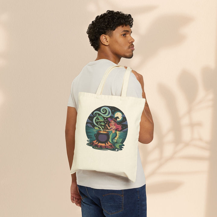 Sea Dragon Dreams natural cotton canvas tote bag featuring a whimsical mermaid cauldron illustration worn over the shoulder