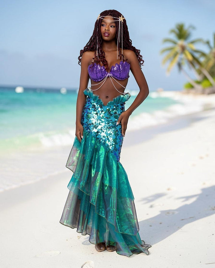Model wearing a Sea Dragon Dreams mermaid costume with a purple sequin shell bra and shimmering green fishtail skirt.