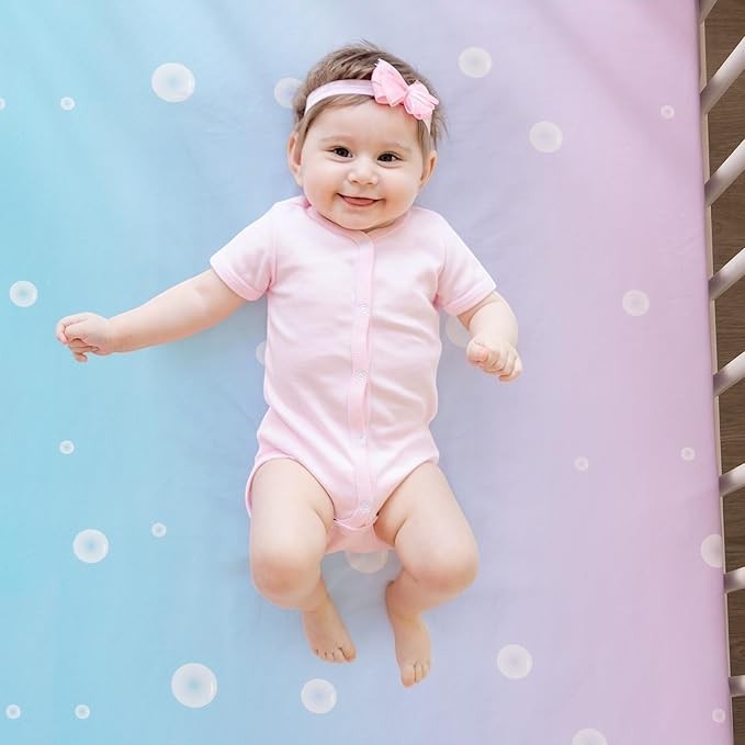 Sea Dragon Dreams mermaid crib bedding set featuring a baby lying on a soft blue and pink ombre bubble-print sheet