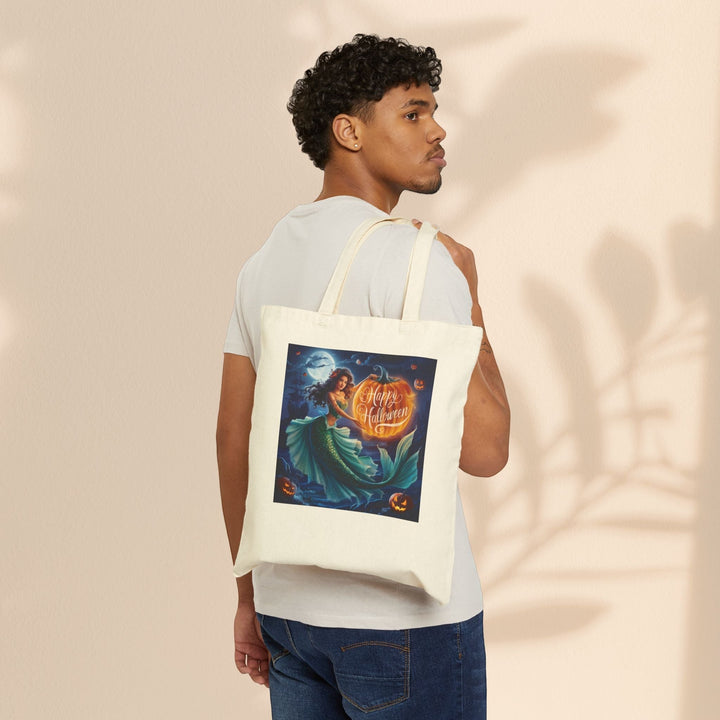 Sea Dragon Dreams natural cotton canvas tote bag featuring a mermaid Halloween graphic worn over a man's shoulder