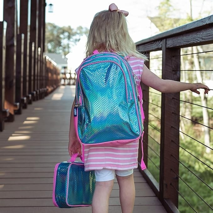 Young girl wearing a Sea Dragon Dreams Wildkin mermaid scales backpack and carrying a matching lunch bag outdoors.