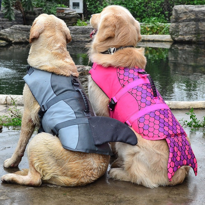 Two golden retrievers wearing Sea Dragon Dreams mermaid and shark dog life jackets with rescue handles by a pond.