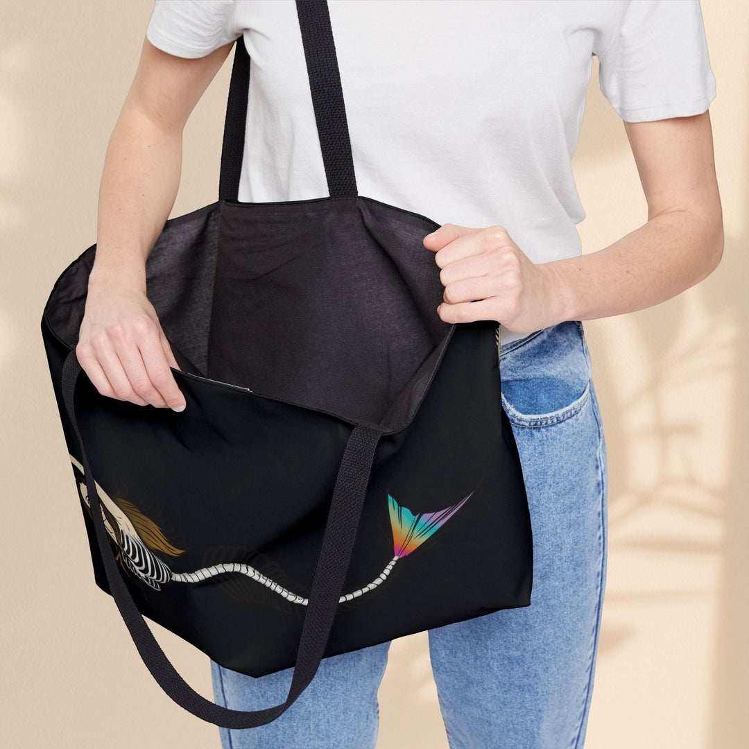 Sea Dragon Dreams mermaid skeleton weekender tote bag with black handles held by a person in a white shirt and jeans