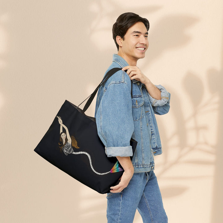 Sea Dragon Dreams weekender tote bag with mermaid skeleton art, carried over the shoulder by a man in a denim jacket.