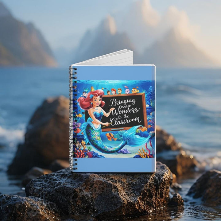 Sea Dragon Dreams spiral notebook featuring a mermaid teacher illustration on a rock against a mountain backdrop.