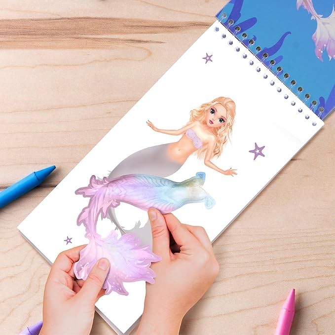 Sea Dragon Dreams mermaid sticker activity book with hands placing a colorful iridescent tail sticker on a model page