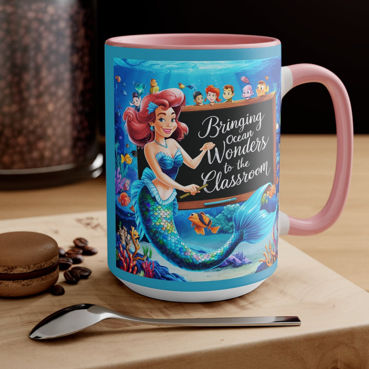 Sea Dragon Dreams ceramic mug with a mermaid teacher illustration and pink handle on a wooden table with a spoon.