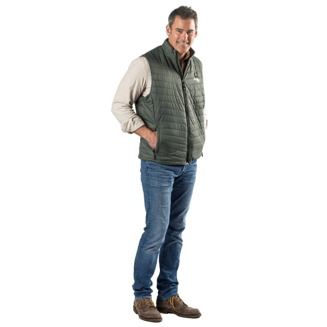 Man wearing a Sea Dragon Dreams moss green Dune heated vest over a beige shirt and jeans, standing against a white background.