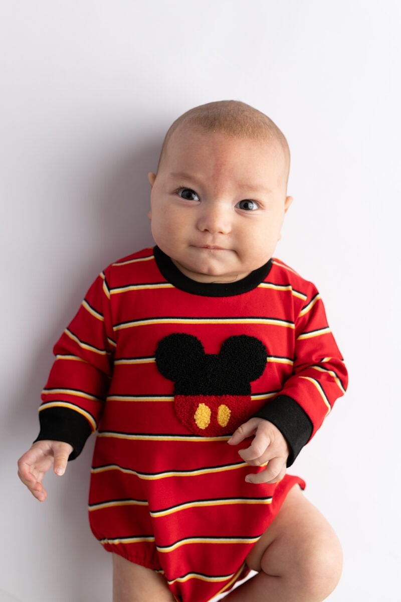 Baby wearing a Sea Dragon Dreams red striped bubble romper with a mouse-inspired applique and black trim.