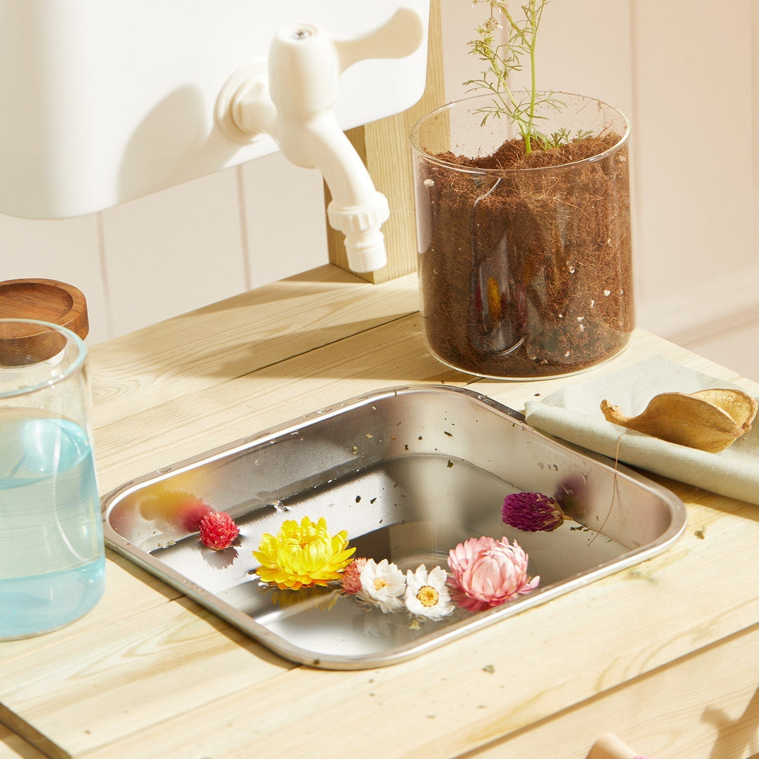 Sea Dragon Dreams Tiny Land mud kitchen sink with a working faucet, filled with water and colorful floating flowers.