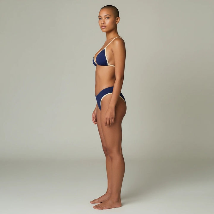 Sea Dragon Dreams navy blue bikini set with contrast trim worn by a model in a side profile view.