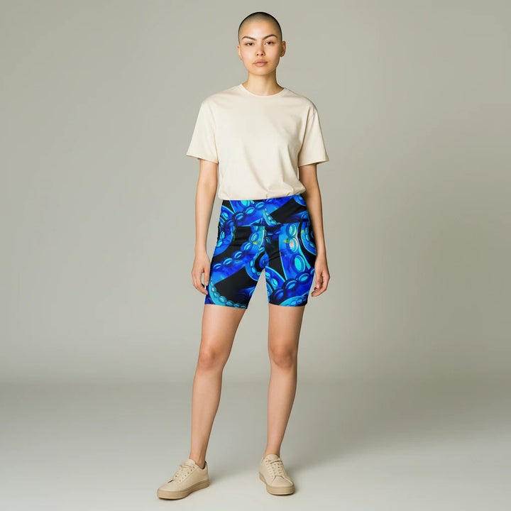 Model wearing Sea Dragon Dreams Octopus Delight workout shorts with a blue octopus tentacle print and beige t-shirt.