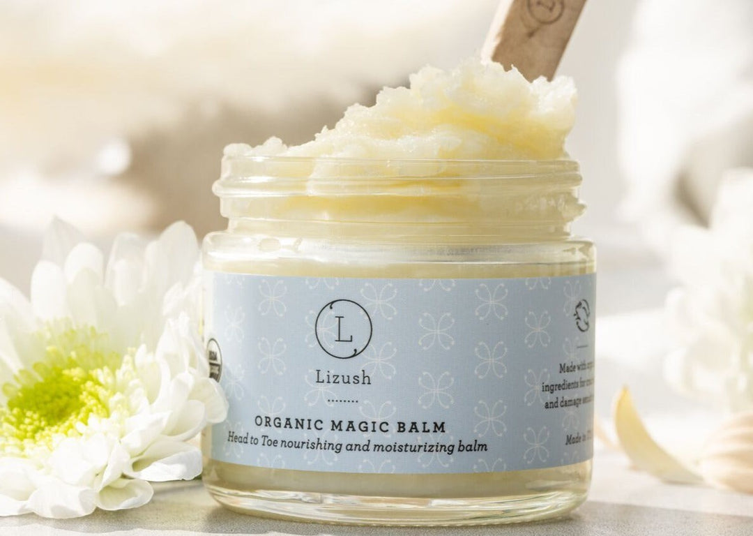 Sea Dragon Dreams organic magic balm in a glass jar with a wooden scoop, surrounded by white flowers.