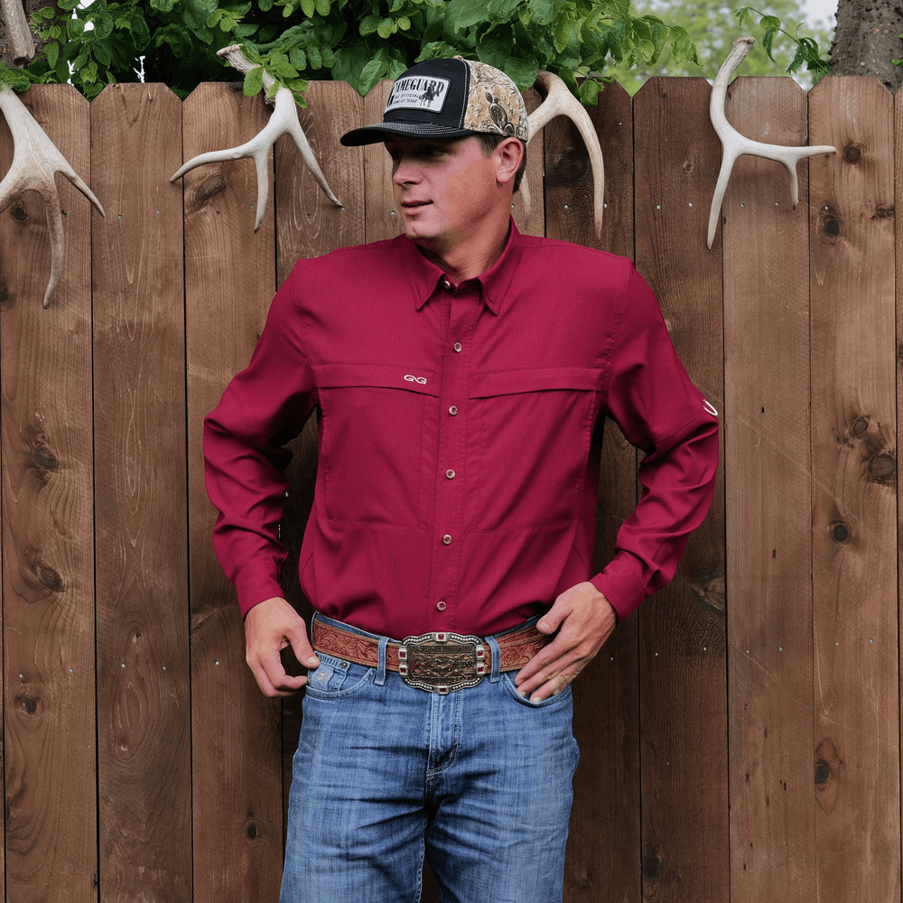 Sea Dragon Dreams oxblood long sleeve scout shirt with hidden chest pockets, worn by a man against a wooden fence.
