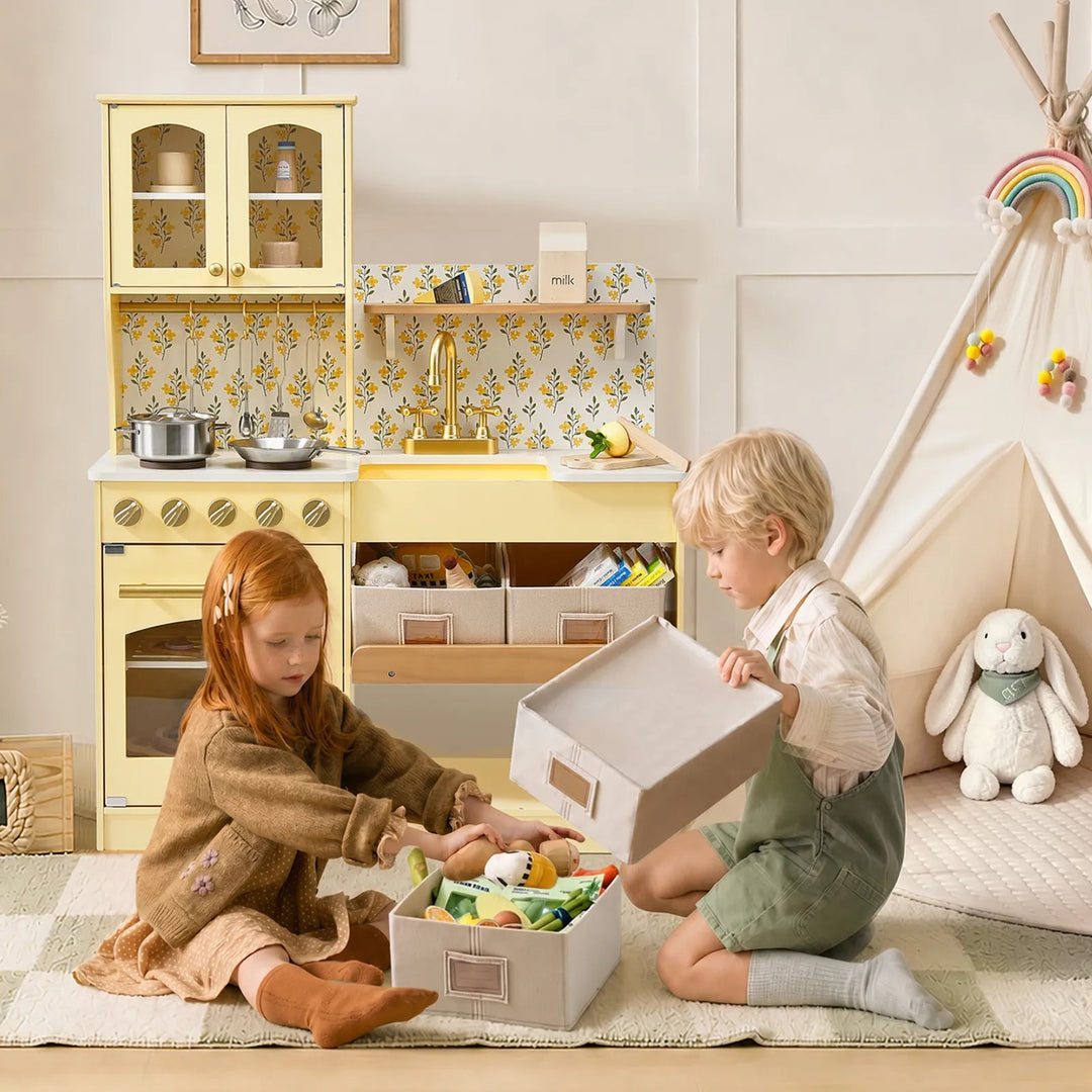 Sea Dragon Dreams pale yellow wooden play kitchen with floral backsplash and storage bins, used by two children.