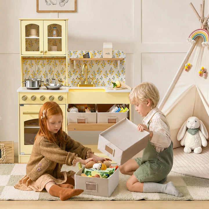 Sea Dragon Dreams pale yellow wooden play kitchen with floral backsplash and storage bins, used by two children.