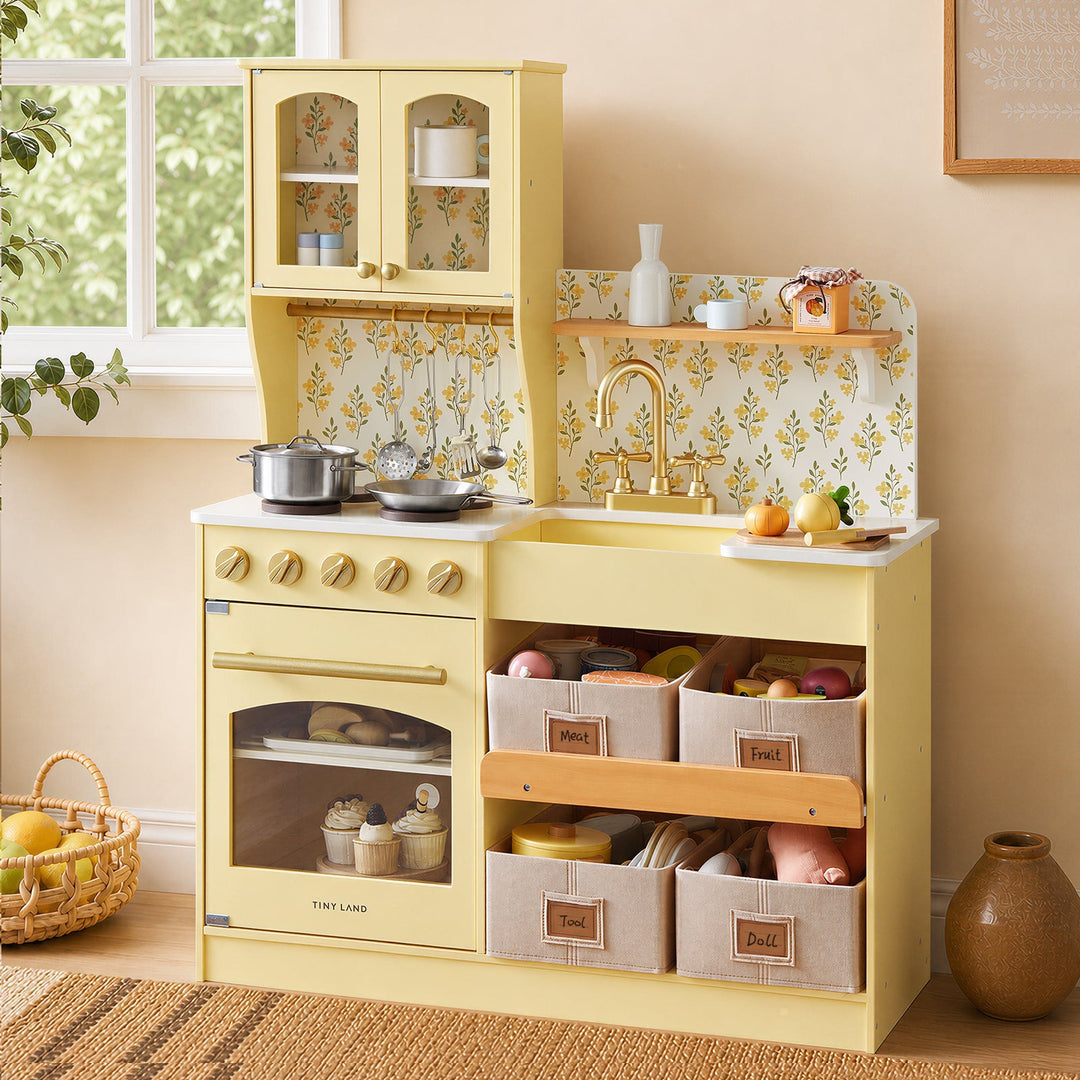 Sea Dragon Dreams Tiny Land wooden play kitchen in pale yellow with floral backsplash, storage bins, and toy cookware.