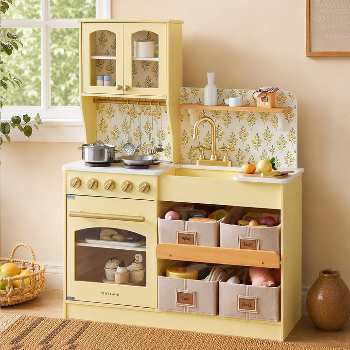 Sea Dragon Dreams Tiny Land wooden play kitchen in pale yellow with floral backsplash, storage bins, and toy cookware.