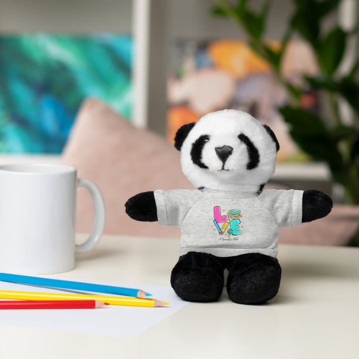 Sea Dragon Dreams panda stuffed animal wearing a grey t-shirt with Love Teacher Life graphic on a desk with pencils