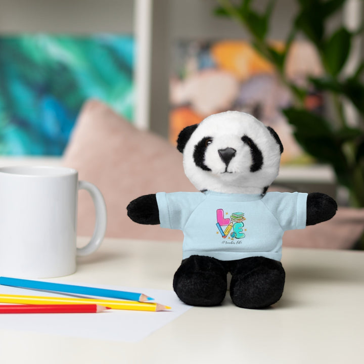 Sea Dragon Dreams panda plush toy wearing a light blue t-shirt with Love Teacher Life graphic on a desk with pencils