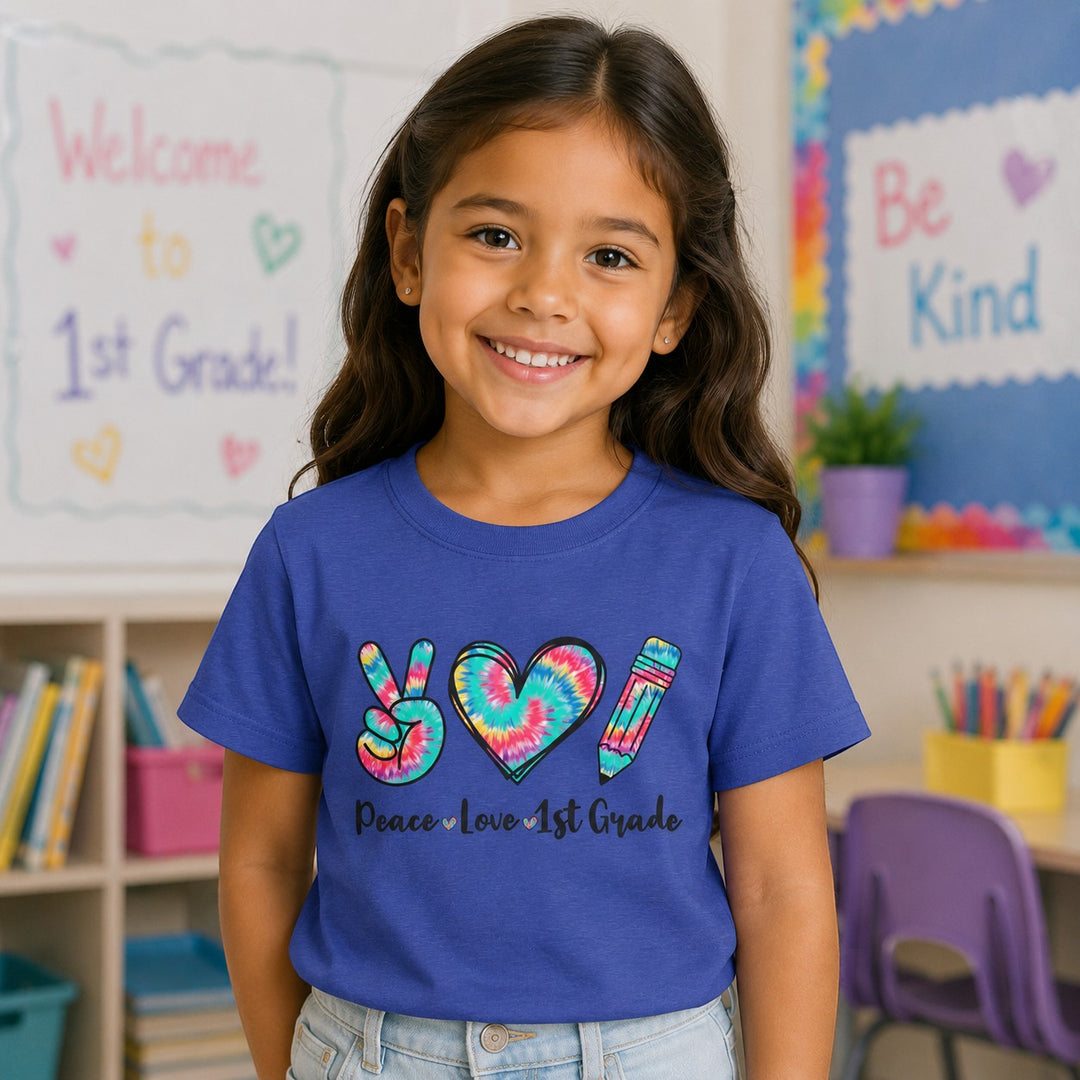 Sea Dragon Dreams youth tee with Peace Love 1st Grade graphic on blue cotton, worn by a smiling girl in a classroom.