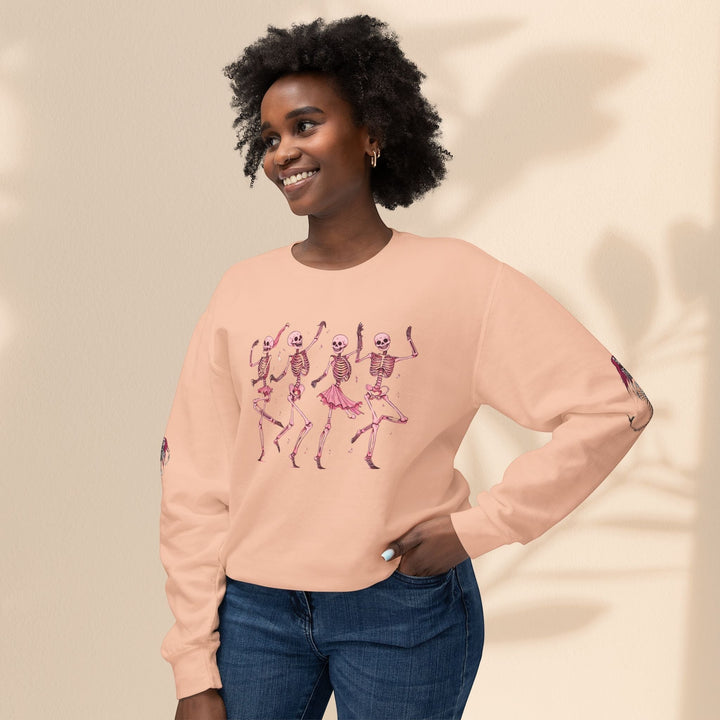 Sea Dragon Dreams peach crewneck sweatshirt with dancing skeletons graphic, worn by a smiling woman in blue jeans.