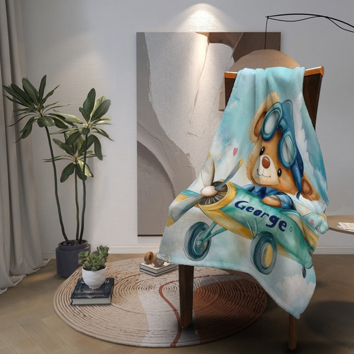 Sea Dragon Dreams personalised fleece blanket featuring a cute teddy bear pilot in a plane, draped over a chair.