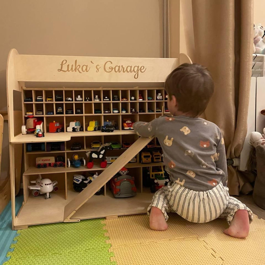 A toddler playing with a personalized Sea Dragon Dreams wooden toy car garage storage unit with multiple shelves.